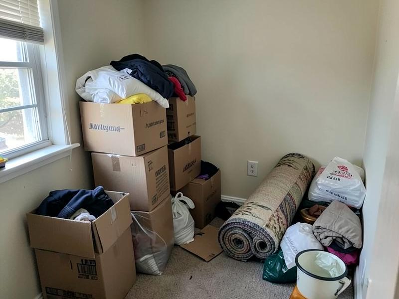 Boxes, bagged clothing and a rolled rug stacked in a spare room